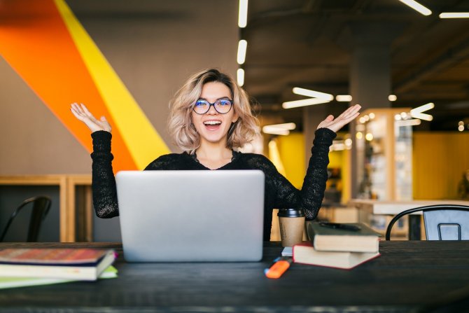 funny-happy-excited-young-pretty-woman-sitting-table-black-shirt-working-laptop-co-working-office-wearing-glasses-scaled.jpg